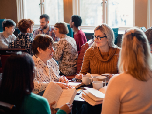 A group of people gathered around tables with coffee and books