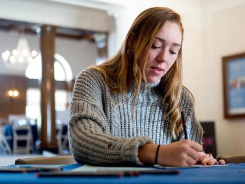 Woman sits at a table writing on a sheet of paper 