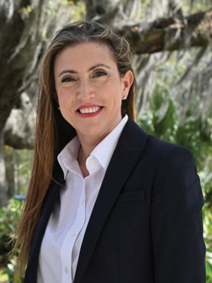 White woman in white shirt and blazer smiles in front of tree with spanish moss