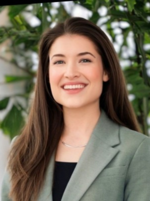 White woman in black shirt and gray blazer smiles in front of tree
