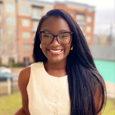 Black woman with glasses in a white dress smiles