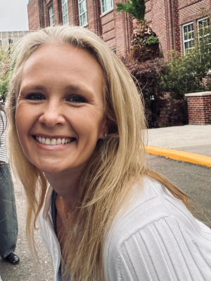 white blonde woman in white shirt in front of bricks smiles